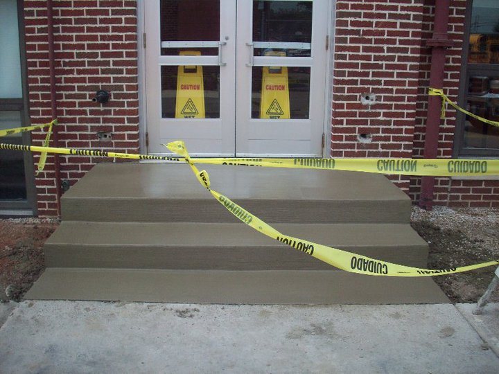 Wide finished concrete entry steps cordoned with caution tape at a red brick commercial building.