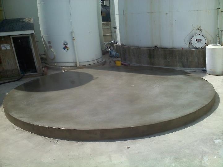 A finished smooth circular concrete tank pad with troweled edge inside an industrial chemical facility.