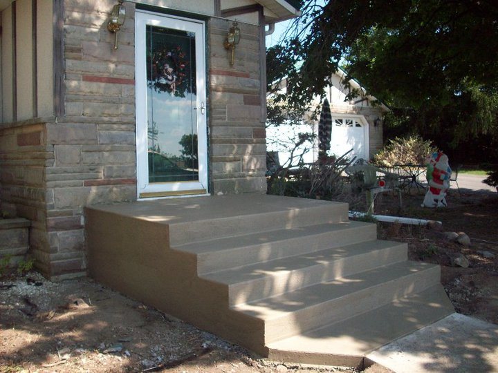 Newly poured plain concrete front entry steps against a stone-faced house.