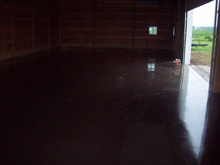 Dark brown stained and sealed concrete floor inside an open pole barn with a glossy finish.