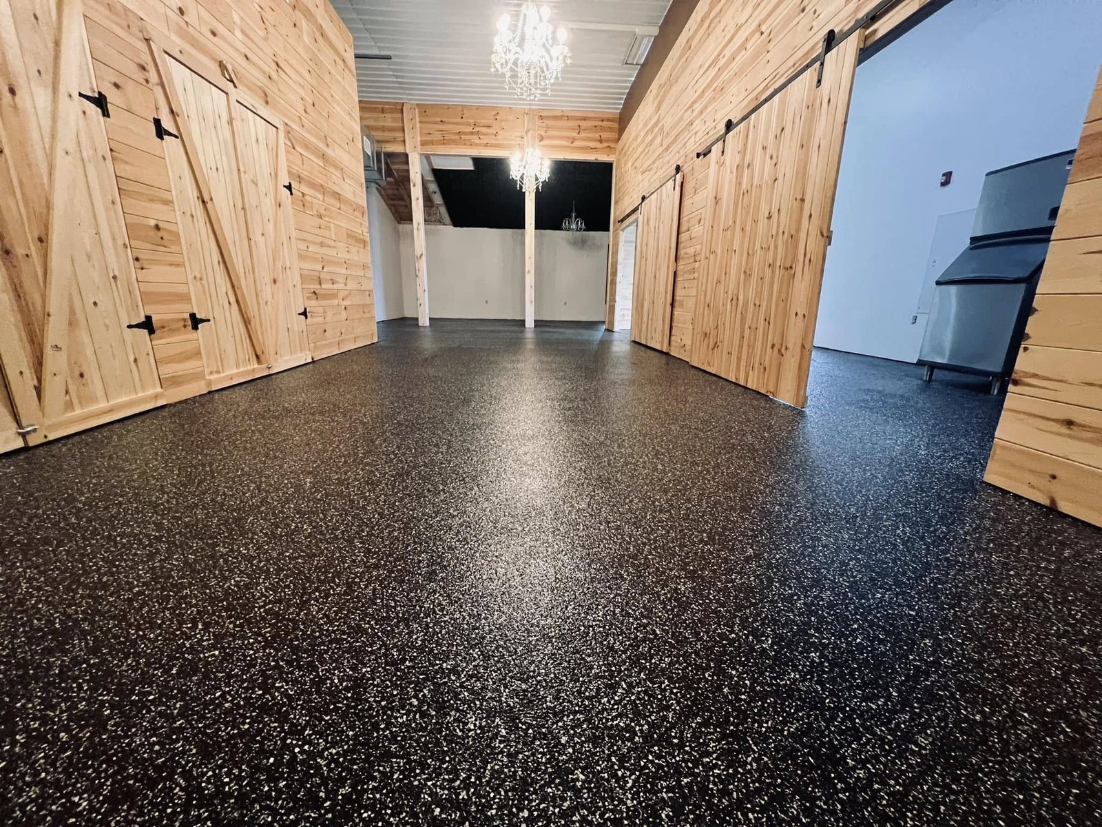 Glossy black and tan flake epoxy floor in an upscale room with barn doors and a chandelier.