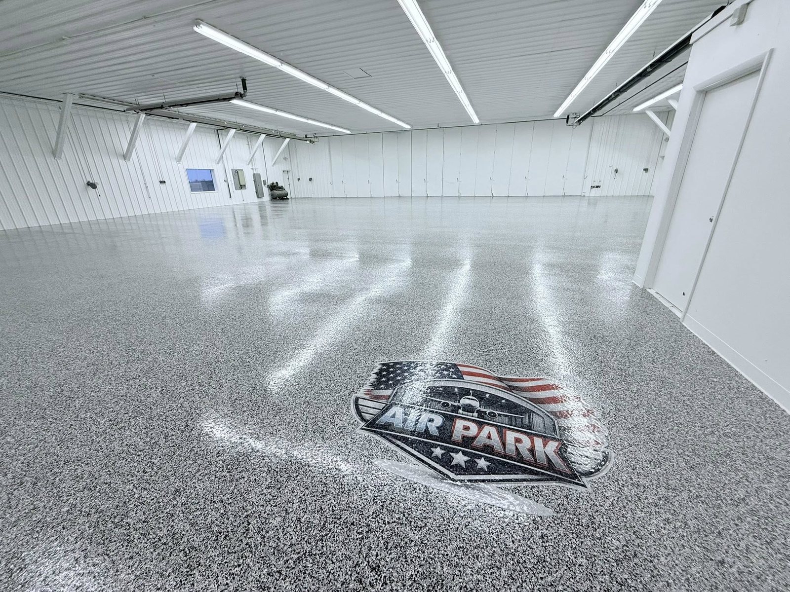 Glossy gray flake epoxy floor with an American-flag logo inlay in a bright hangar.