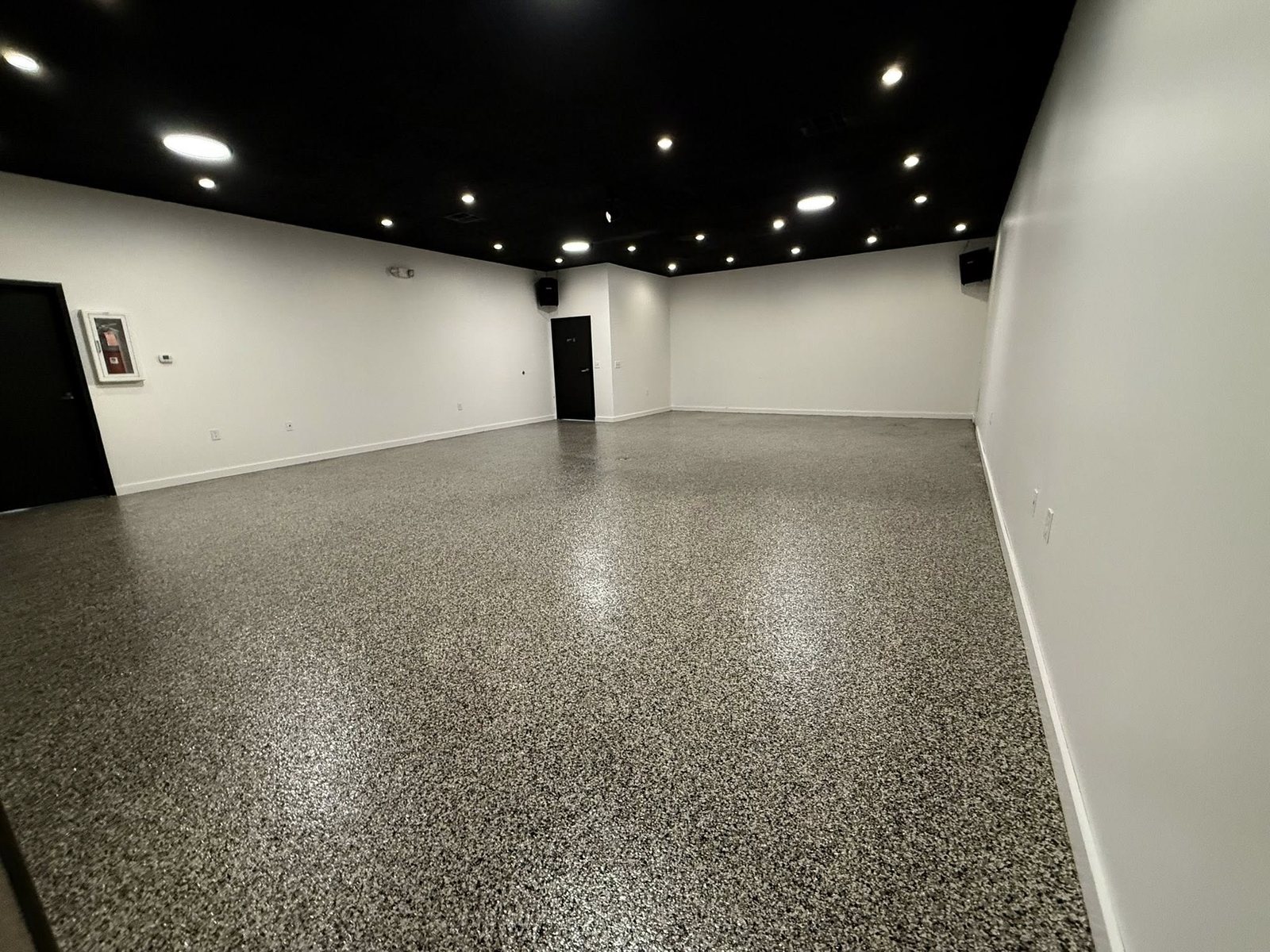 Tan, gray and black flake epoxy floor in a commercial space with recessed lighting.
