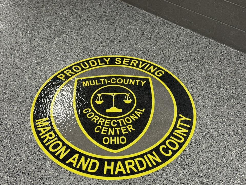 Gray flake epoxy floor with an inlaid facility logo medallion.
