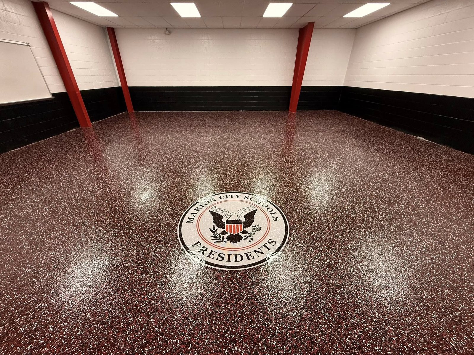 Maroon and white flake epoxy floor with an inlaid Presidents school medallion.