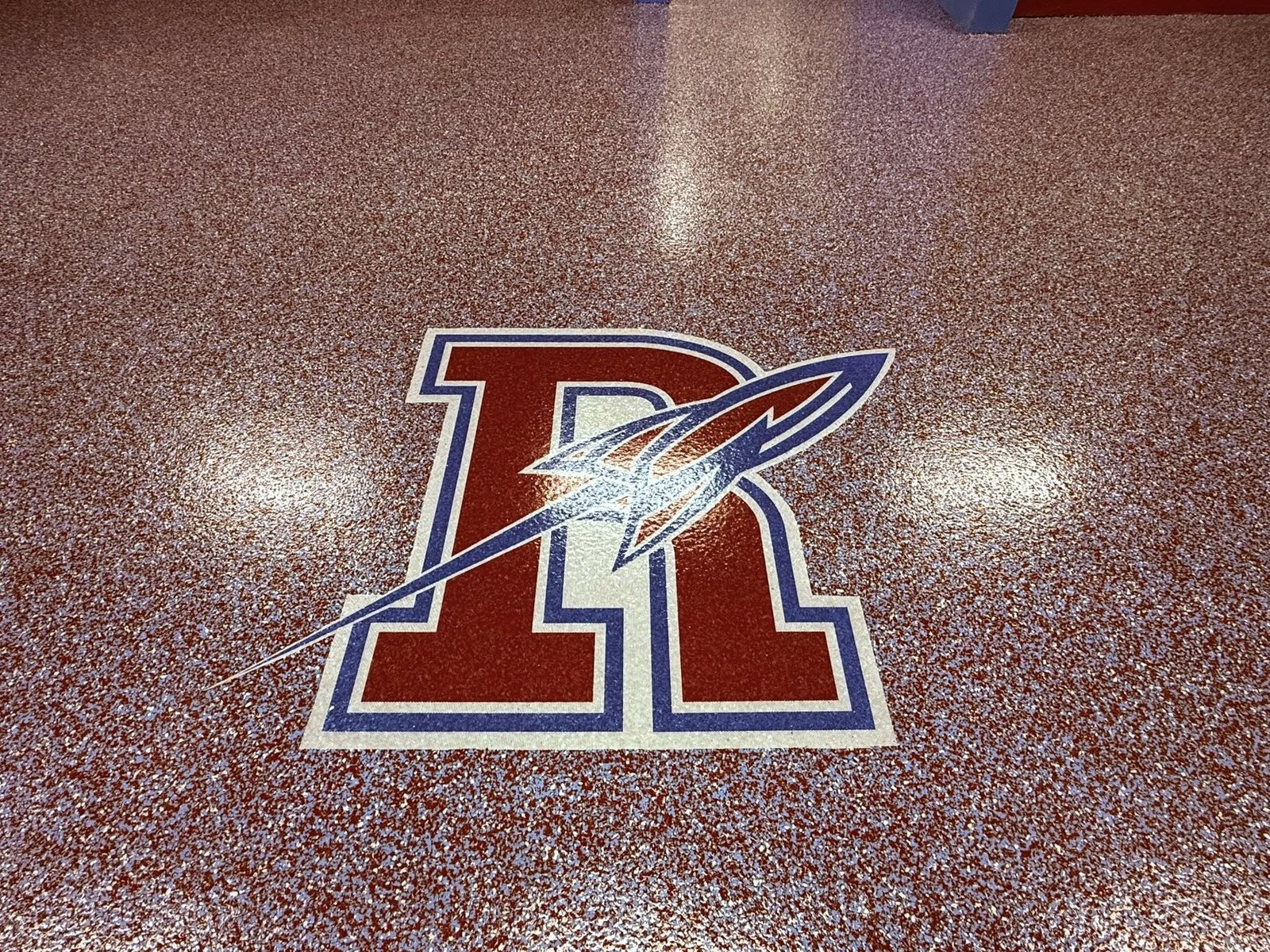 Red and tan flake epoxy floor with an inlaid team rocket-logo medallion.