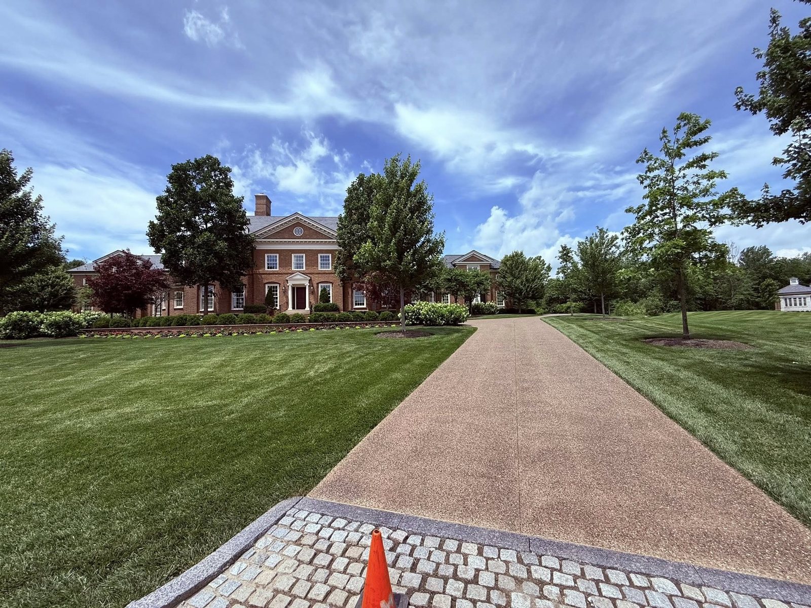 Exposed-aggregate concrete driveway with a cobblestone border at a brick estate.