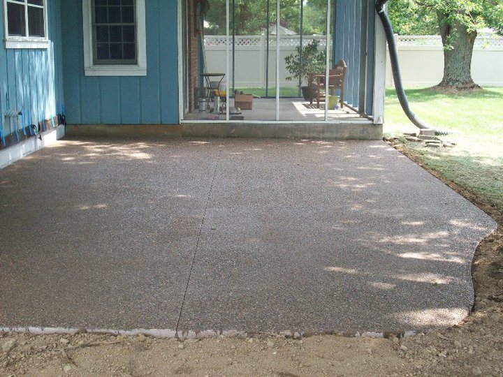 The same blue house backyard with a finished exposed-aggregate concrete patio