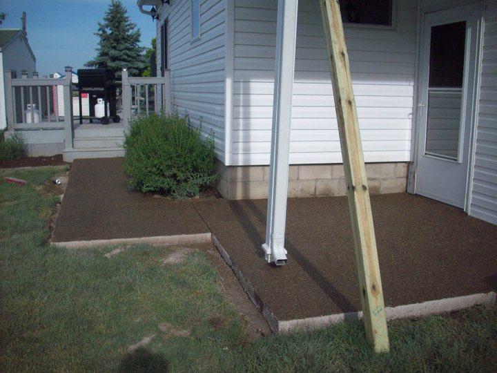 Freshly finished exposed aggregate concrete patio along the side of a gray sided house with form boards still in place.