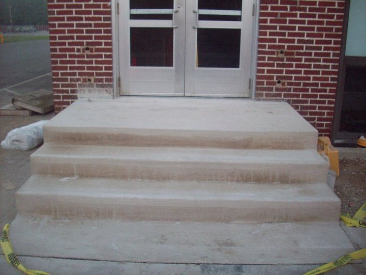 Cured plain concrete entrance steps at a red brick commercial building doorway.