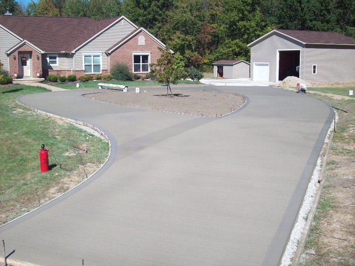 Freshly poured broom-finished concrete circular driveway with center planting island in front of a brick ranch home and garage.