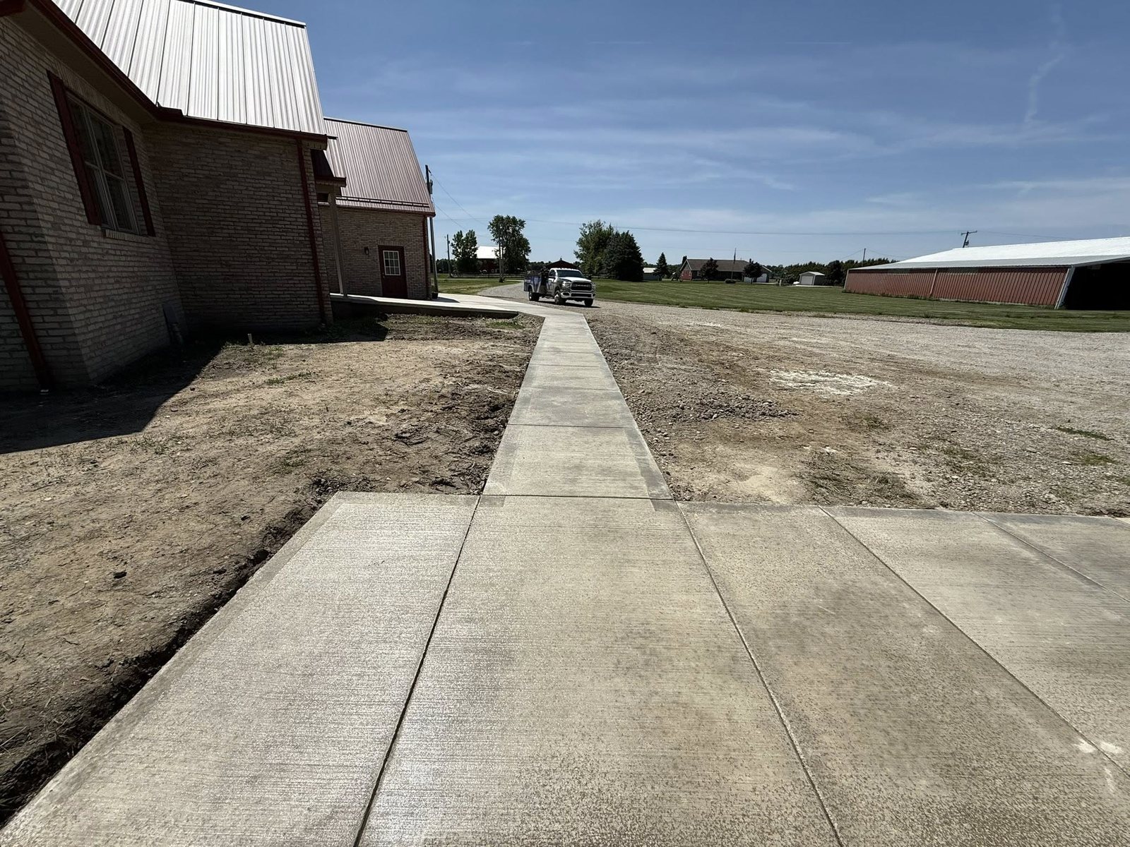 Long concrete sidewalk running beside a brick building on a rural property.