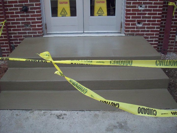 Freshly finished concrete entrance steps taped off at a brick commercial building doorway.