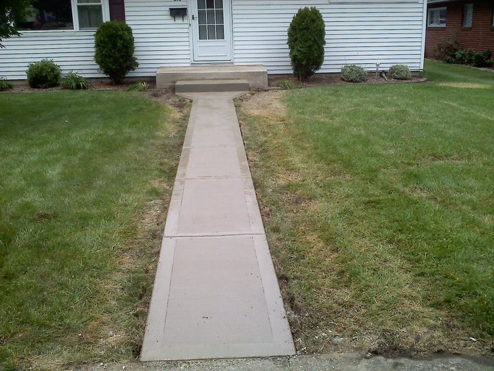 Plain tan concrete front walkway and step poured up to the entry door of a white sided house.