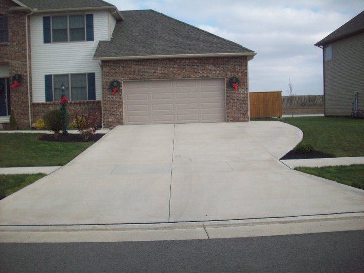 A finished plain concrete driveway leading to a two-car garage of a brick home decorated with Christmas wreaths.