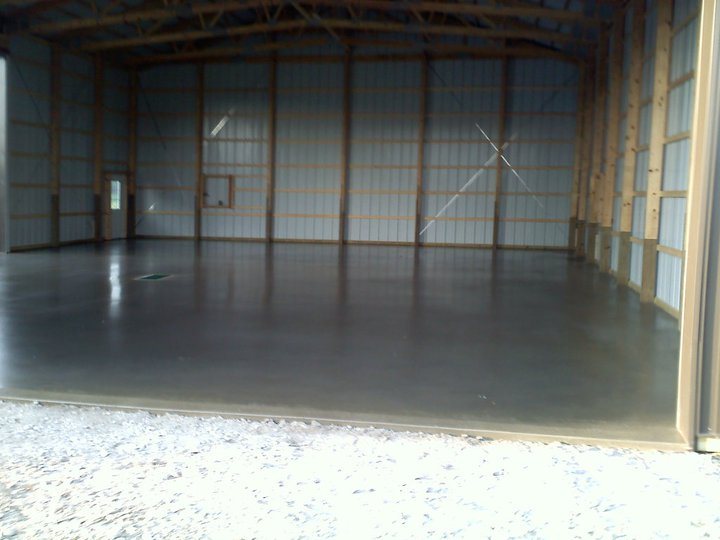 Smooth finished gray concrete floor slab inside a large empty steel-and-wood pole barn.