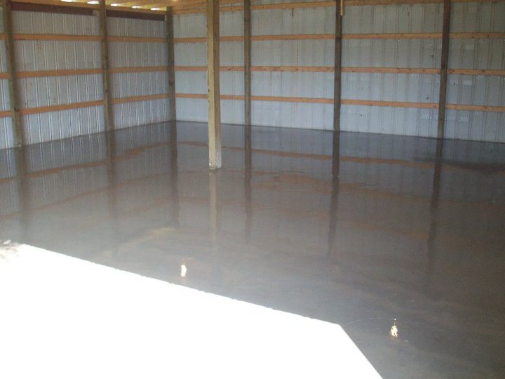 Freshly poured concrete floor with a wet curing sheen inside a metal pole barn with wood-framed walls.