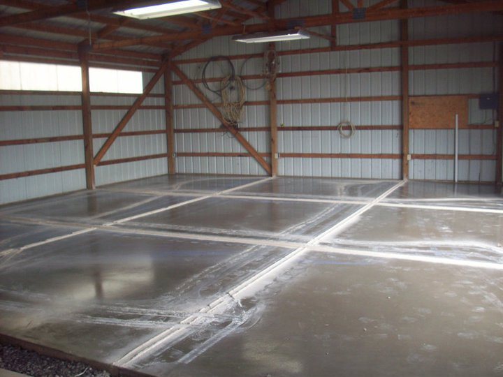 Freshly poured and saw-cut concrete garage slab curing inside a wood-framed metal pole barn.