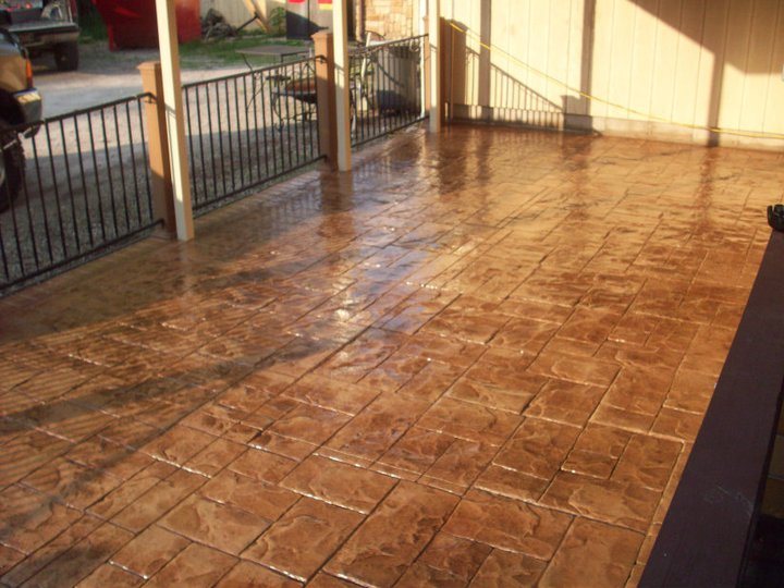 Glossy sealed tan stamped concrete patio with an iron railing under a covered porch area.