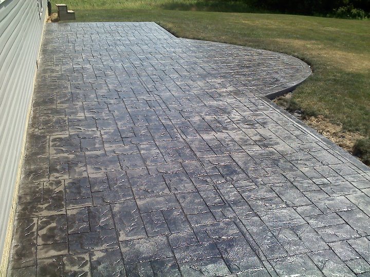 A finished gray stamped concrete patio with ashlar slate texture and rounded edge beside a home.