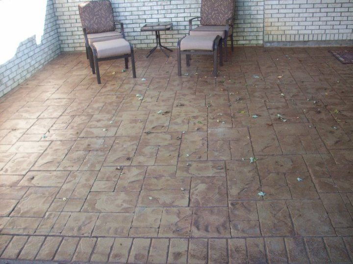 Tan stamped concrete courtyard patio with an ashlar pattern, enclosed by light brick walls and furnished with patio chairs.