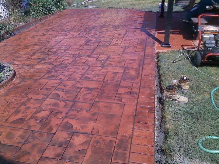 Freshly sealed stamped concrete patio in an ashlar pattern with rich red-brown stain, still wet and glossy.