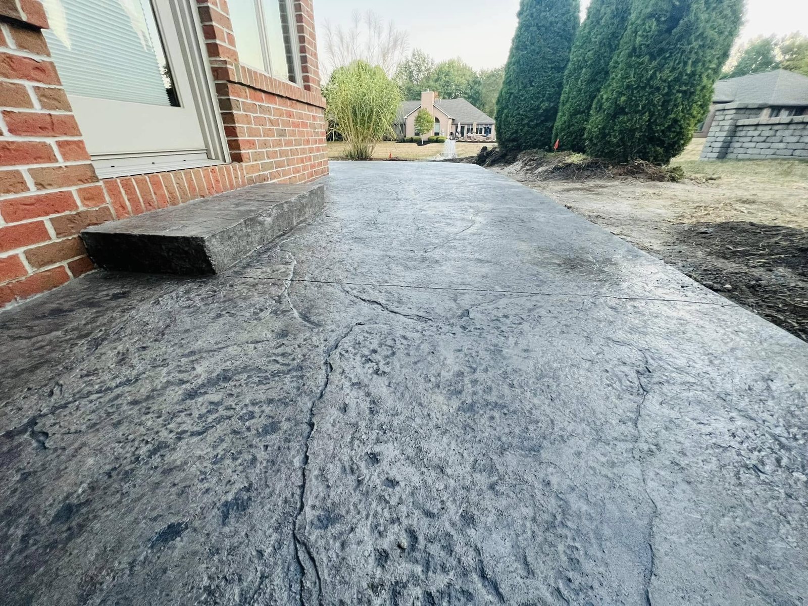 Gray seamless slate-textured stamped concrete patio with a step at a brick home.