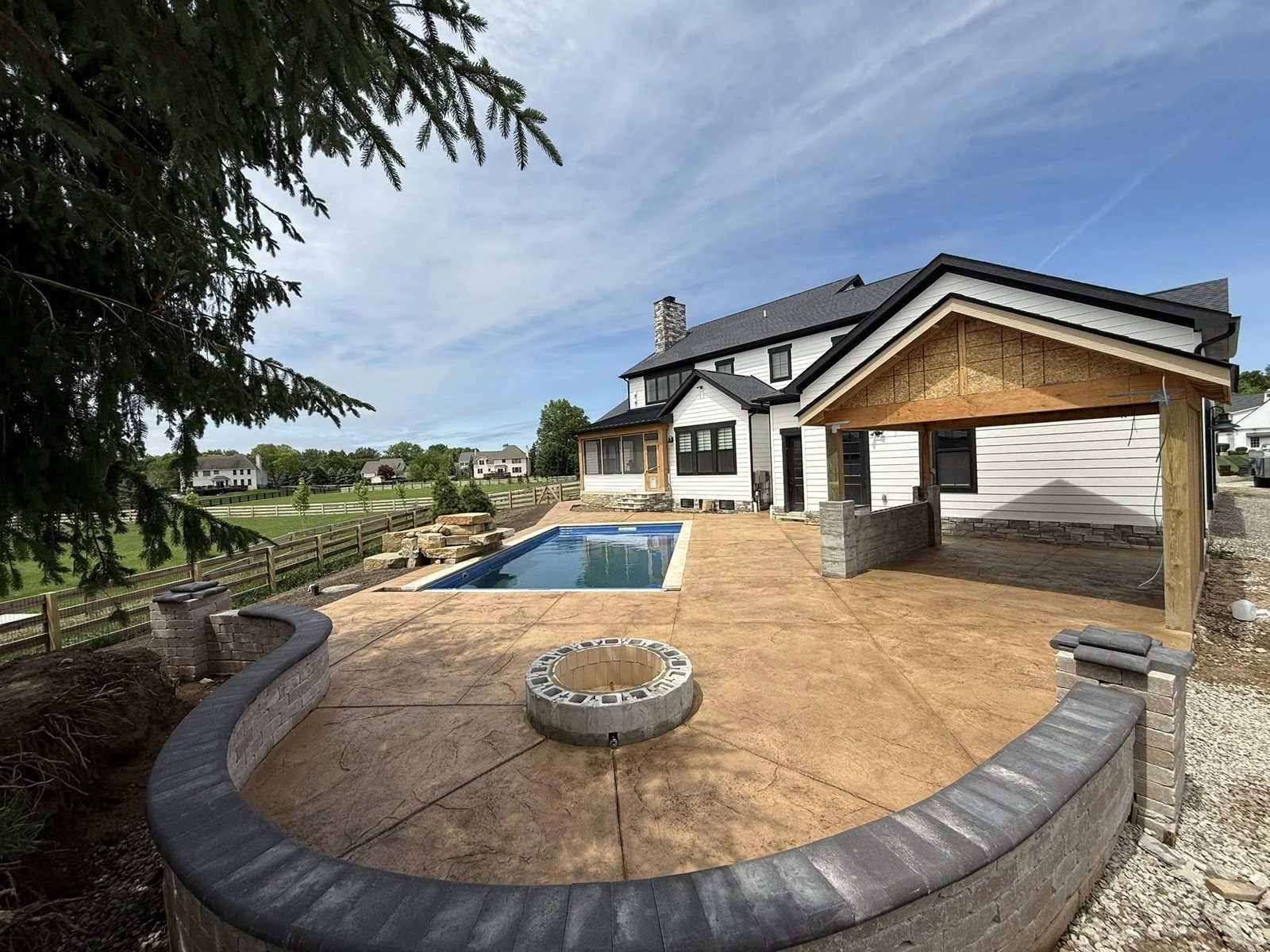 Stamped concrete patio with a fire pit and seating wall beside a backyard pool.