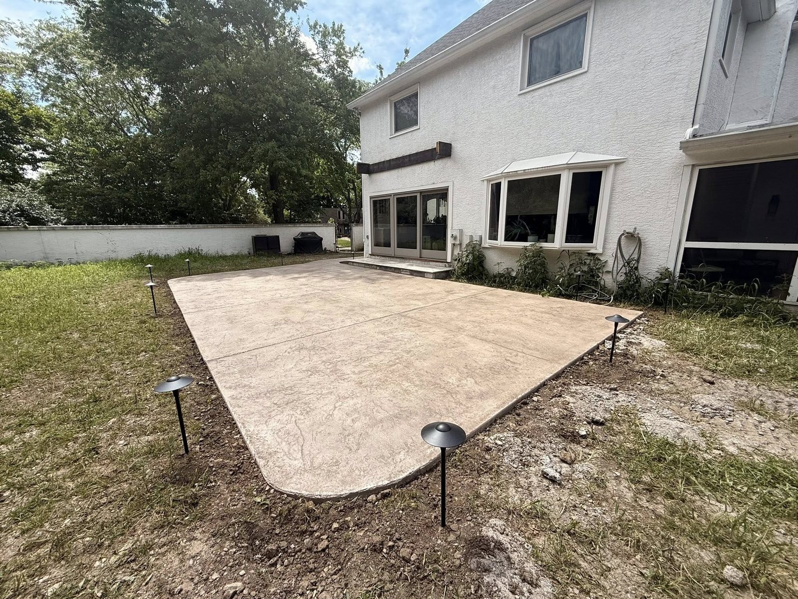 Tan textured stamped concrete patio behind a white two-story home.