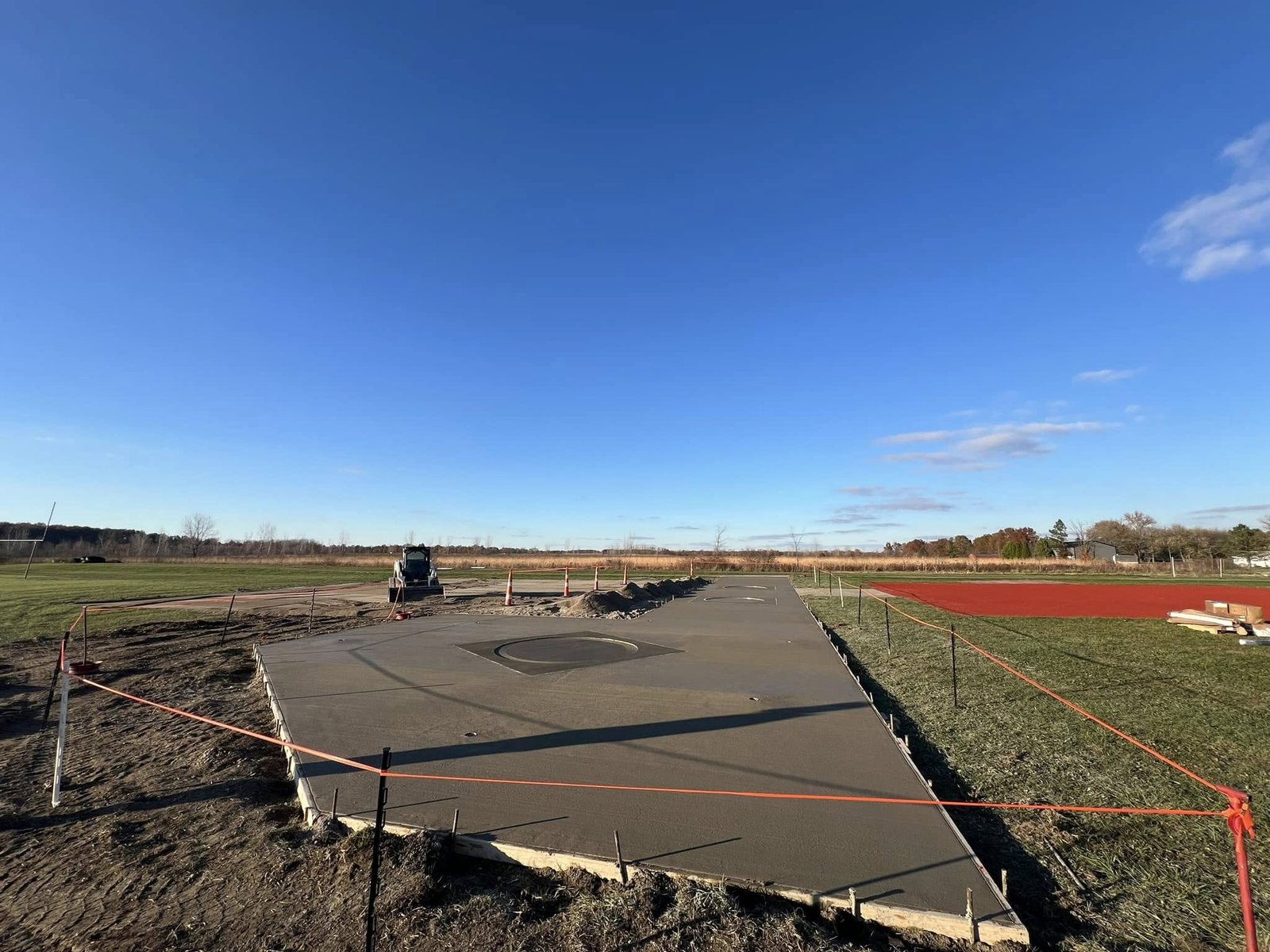Freshly finished concrete shot-put and discus pad with an inset ring beside a red running track.