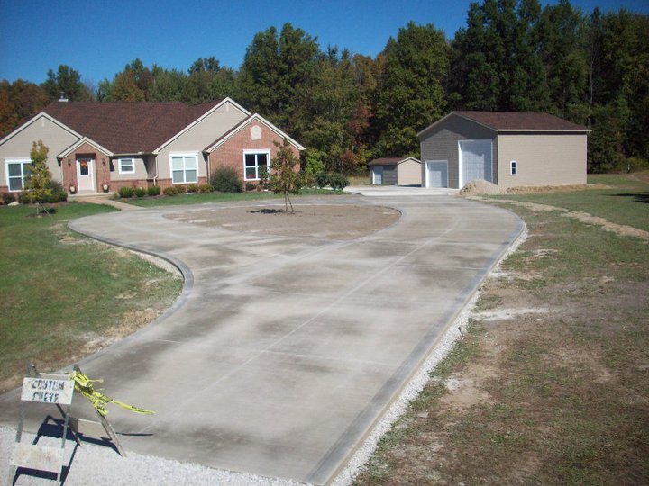 A large finished plain concrete circular driveway in front of a brick ranch house and detached garage with a Custom Crete yard sign.
